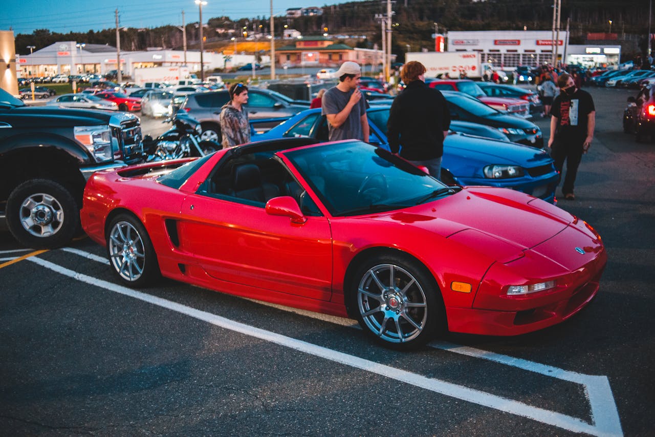 A striking red Acura NSX convertible parked among enthusiasts at an evening car meetup showcasing luxury and style.